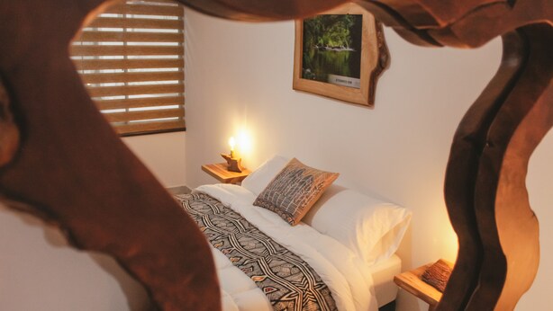A bedroom with a bed, a bedside table with a lamp, a framed picture on the wall, and a window with blinds. - Nogal Hostel (Pereira)