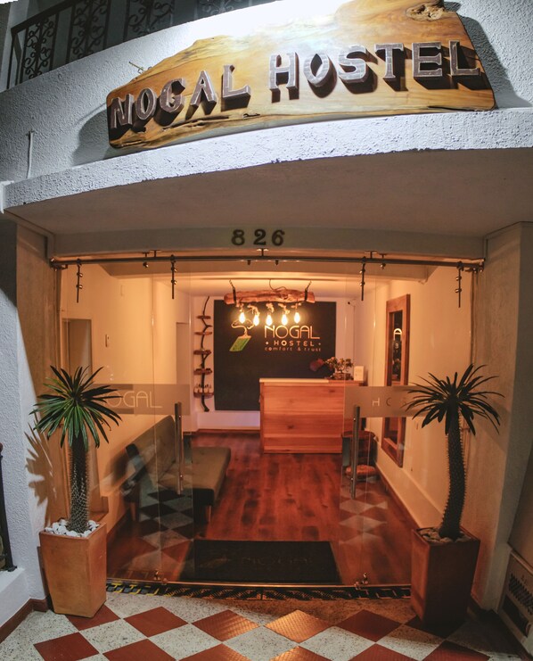 Un letrero de madera con la inscripción "NOGAL HOSTEL" y el número "826" sobre un mostrador de recepción.