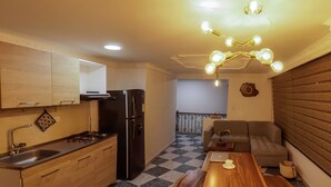 A compact kitchen with a gas stove, sink, and black refrigerator. There's a dining area with a wooden table and a sofa. - Nogal Hostel (Pereira)