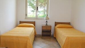 A bedroom with two single beds, a nightstand, a lamp, and a window with a view of greenery. - Villa Faro with panoramic garden and barbecue. 350m from the sea (RICADI)