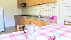 A kitchen with wooden cabinets, a sink, and a table set with a pink tablecloth, a coffee pot, and a vase with flowers. - Villa Faro with panoramic garden and barbecue. 350m from the sea (RICADI)
