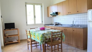 Una pequeña cocina con armarios de madera, salpicadero de azulejos, una ventana y una mesa de comedor con sillas.