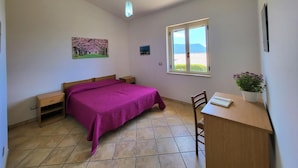 Un dormitorio con cama, escritorio, silla, ventana con vistas y una lámpara colgante.