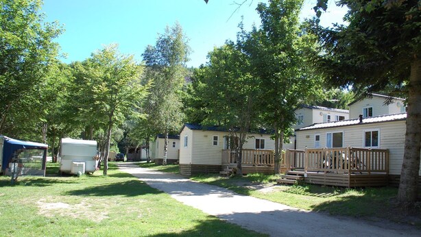 A row of mobile homes with wooden decks and a gravel path between them. - Camping Les Airelles (Saint-Cirgues-en-Montagne)