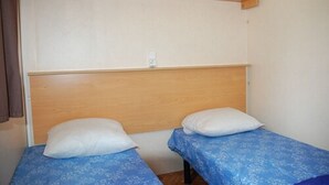 A small room with two single beds, each with a blue patterned bedspread and white pillows. - Camping Les Airelles (Saint-Cirgues-en-Montagne)