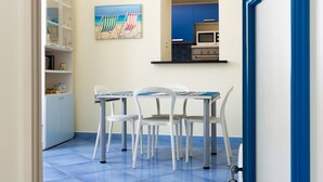 Ein Zimmer mit blau gefliestem Boden, einem weißen Schrank mit Glastüren, einem Bild von Strandstühlen und einer Küchenzeile.