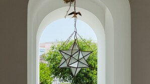 Ein sternförmiger hängender Schmuck an einem weißen, bogenförmigen Durchgang, der zu einem Garten mit verschiedenen Pflanzen und einer Steinmauer führt.