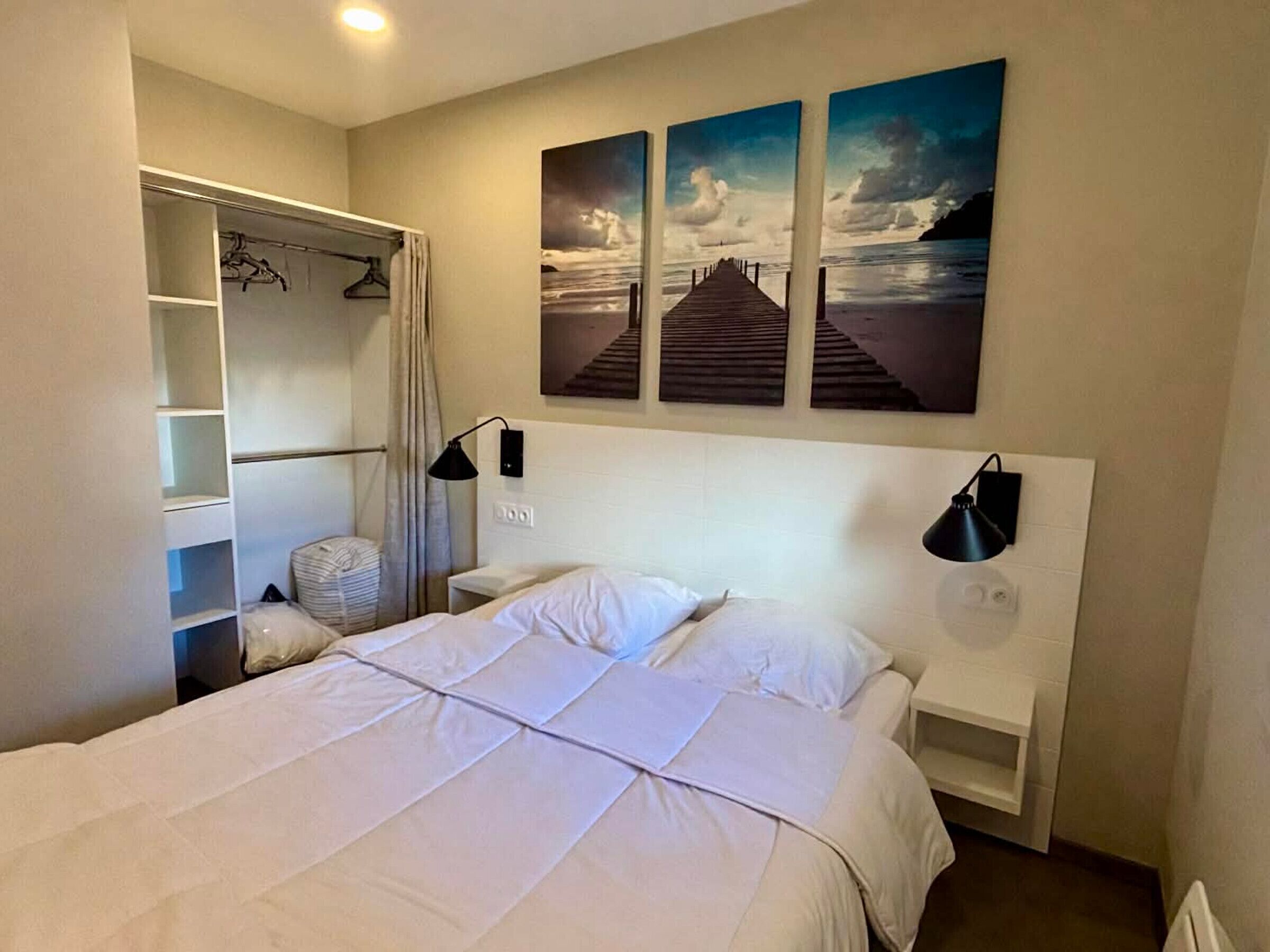 A hotel room with a bed, a wardrobe, a headboard with artwork, and a nightstand.