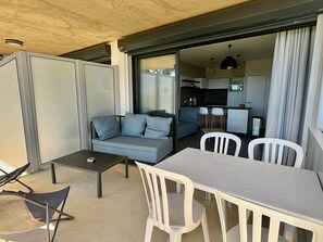 Uma área externa moderna com um sofá, cadeiras, uma mesa e uma cozinha ao fundo.