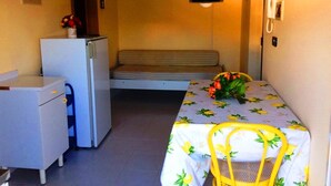 Une chambre de taille modeste, équipée d’un lit, d’un petit bureau, d’un réfrigérateur et d’un téléviseur fixé au mur.