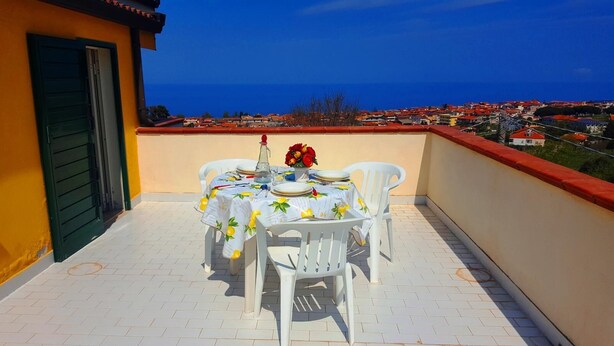 Un balcon avec une table dressée pour deux personnes, donnant sur une ville côtière.