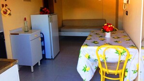 Une chambre de taille modeste, comprenant un lit, un petit bureau, un réfrigérateur, un téléviseur fixé au mur et un téléphone.