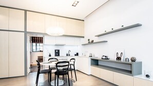 Een moderne keuken met een eethoek, met lichte kasten, een ronde eettafel met stoelen en een hanglamp.