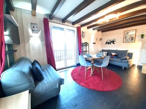 A living room with a sofa, a dining table with chairs, a red rug, and a balcony with red curtains.