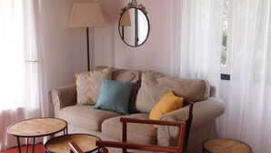 Una sala de estar con un sofá color beige, dos mesas redondas de madera, una lámpara de pie y un espejo en la pared.