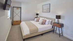 A bedroom with a bed, bedside tables, a TV, a door, and a framed picture on the wall. - Host & Stay | The View, Hudsons Yard House (Whitby)