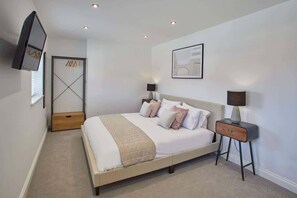 A bedroom with a bed, bedside tables, a TV, a door, and a framed picture on the wall.