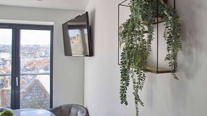 A modern room with a large window, a flat-screen TV, a hanging plant, and a round table. - Host & Stay | The View, Hudsons Yard House (Whitby)