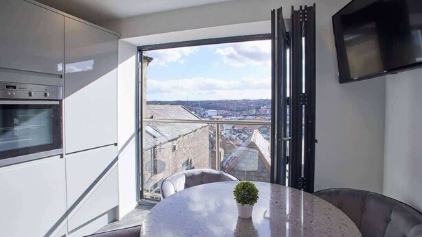 A modern kitchen with a built-in oven, a dining area with a round table and chairs, and a large window offering a city view. - Host & Stay | The View, Hudsons Yard House (Whitby)