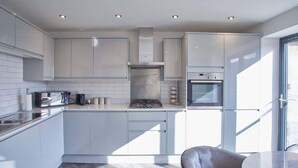A modern kitchen with white cabinetry, a built-in stove, and a dining area with a round table and a chair. - Host & Stay | The View, Hudsons Yard House (Whitby)