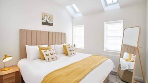 Une chambre à coucher avec un grand lit, une table de chevet avec une lampe, un miroir et un tableau au mur.