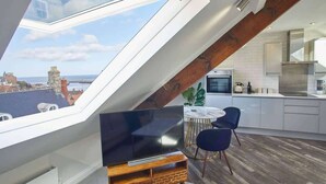 A modern kitchen with a large window, a flat-screen TV, and a dining area with chairs. - Host & Stay | The Penthouse, Hudsons Yard House (Whitby)
