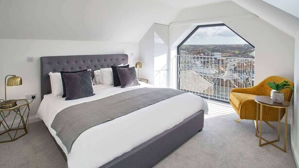 A modern bedroom with a large bed, a small side table, a chair, and a balcony with a city view. - Host & Stay | The Penthouse, Hudsons Yard House (Whitby)