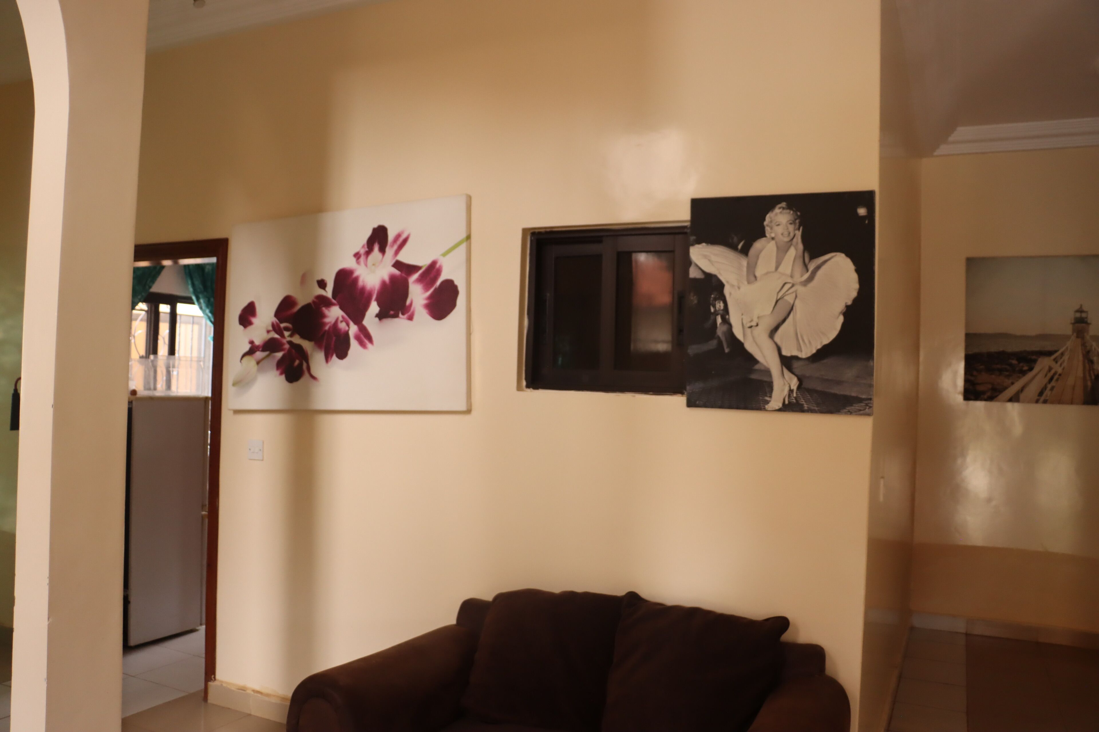 Een woonkamer met een bruine bank, een aan de muur bevestigde televisie en een bloemschilderij.