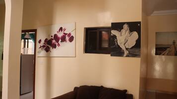 Een woonkamer met een bruine bank, een aan de muur bevestigde televisie en een bloemschilderij.