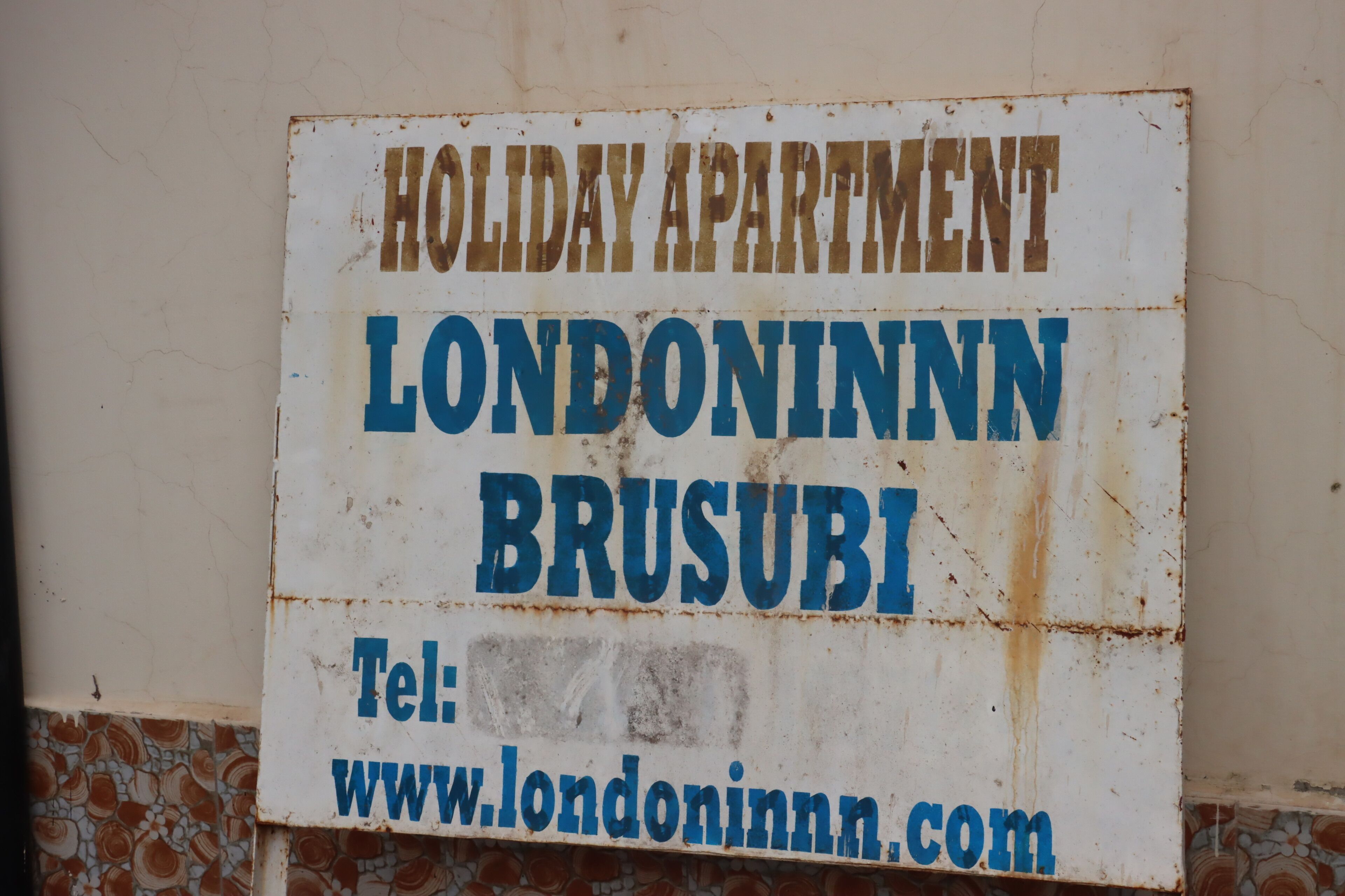 Letrero de un apartamento vacacional en Londoninnn Brusubi, que incluye una dirección web y un número de teléfono.