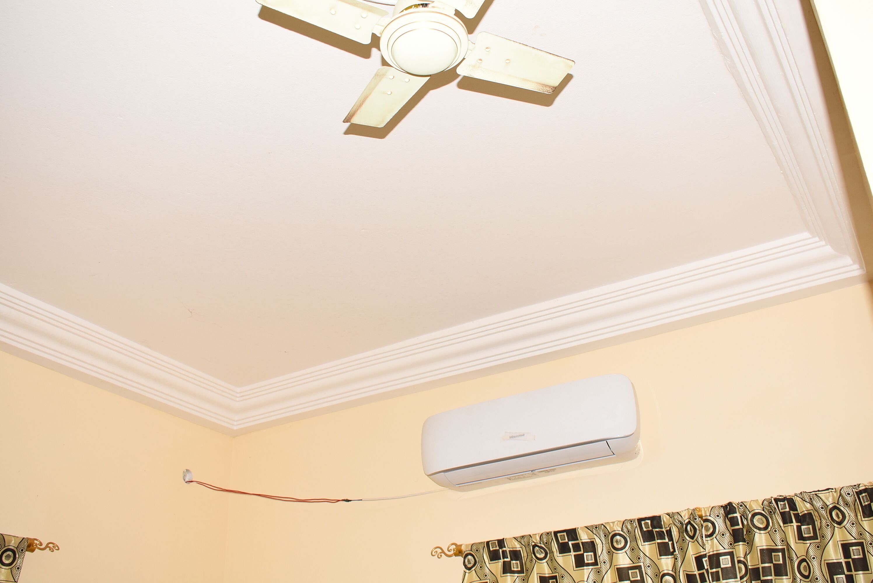 Un ventilateur de plafond, un climatiseur et un rideau à motifs.