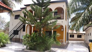 Un edificio de dos pisos con un patio empedrado, una escalera y un árbol grande en el centro.