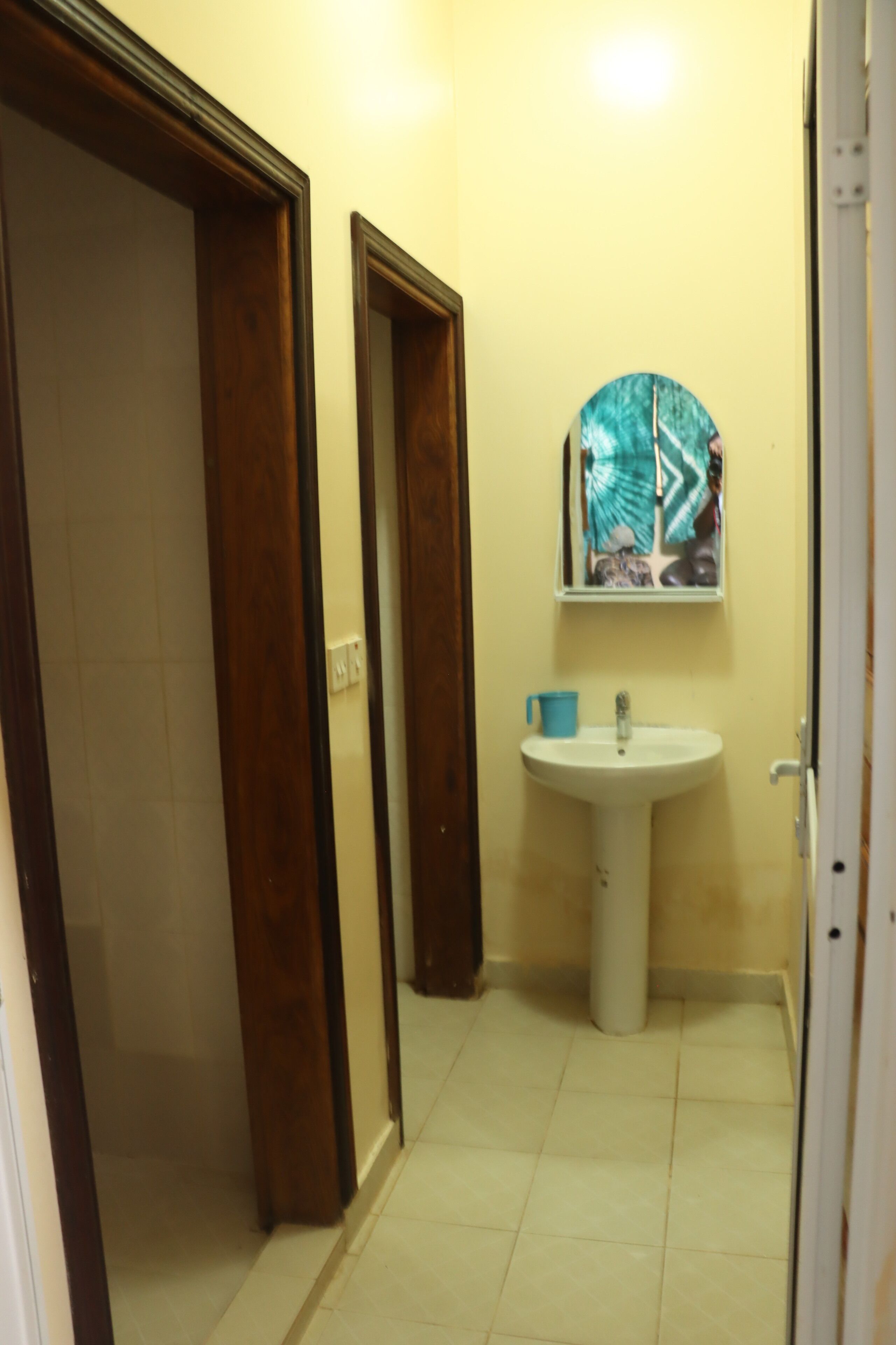 Een badkamer met een wit wastafelmeubel, een spiegel en een blauw kopje op het aanrecht.