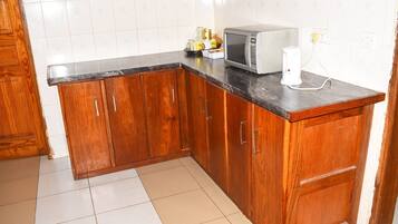 A kitchen with wooden cabinets, a microwave, and a kettle on the countertop.