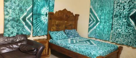 A bedroom with a wooden bed, a brown leather sofa, and patterned curtains.