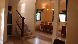 Una escalera conduce a un comedor con una araña, una ventana con cortinas y una puerta.