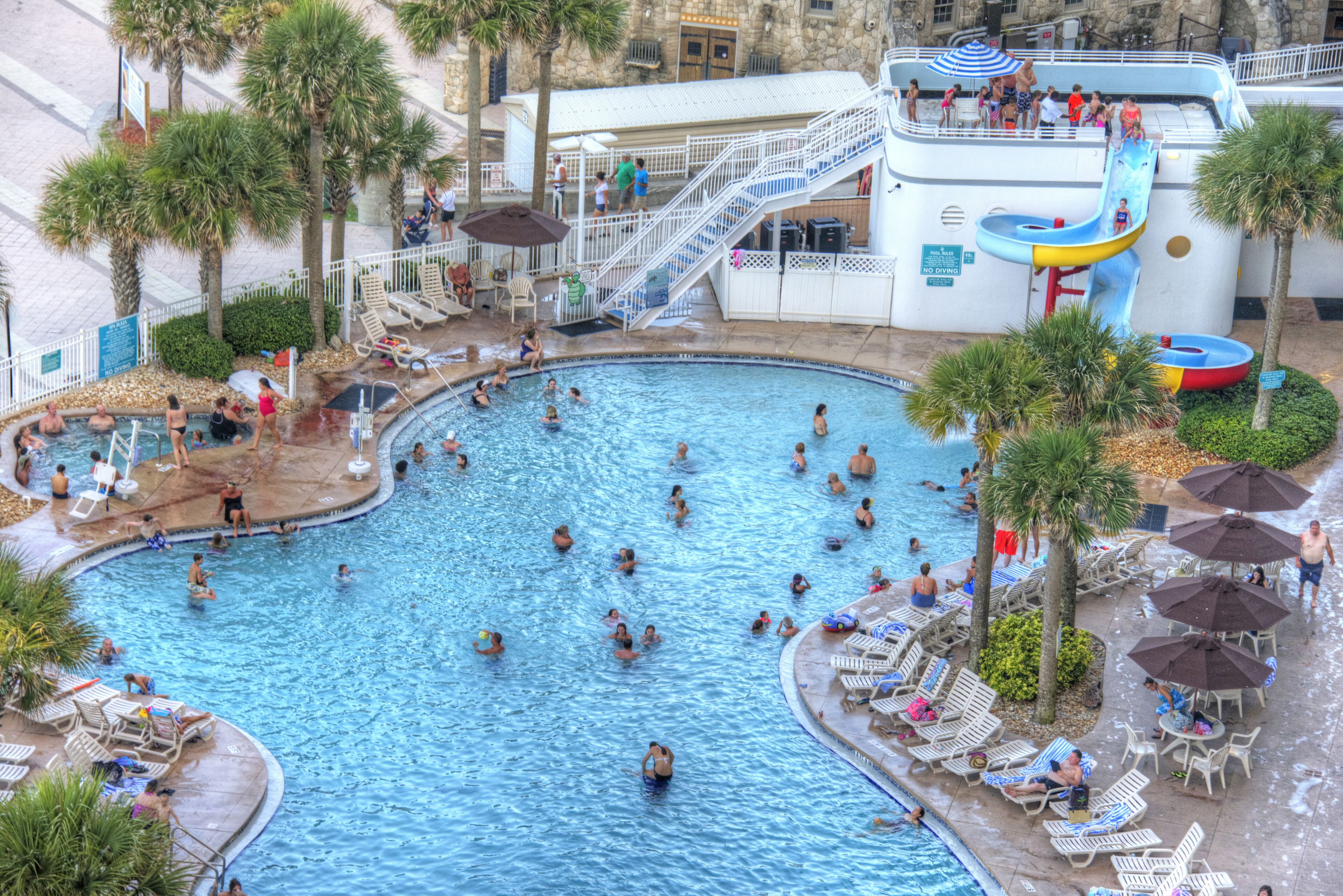 Una amplia piscina interior con varias pistas, rodeada de palmeras y tumbonas.