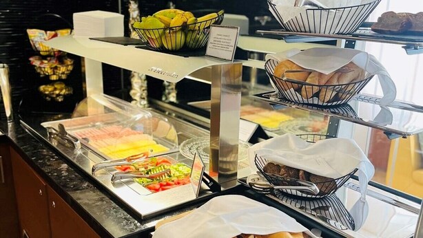 Mostrador de buffet con diversos alimentos, como frutas, pasteles y sándwiches.