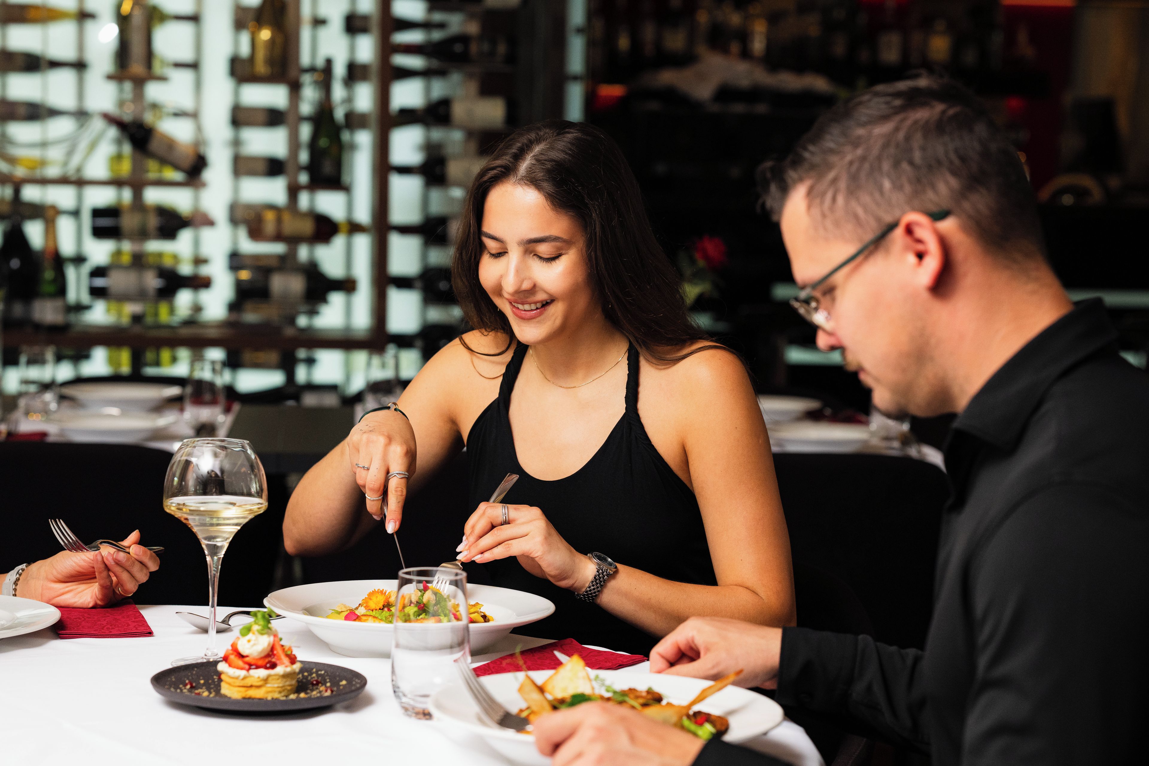 A dining table with plates of food, a wine glass, and a bottle of water.