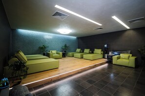 Un área de descanso moderna con sofás verdes, piso de madera y pared con azulejos azules.