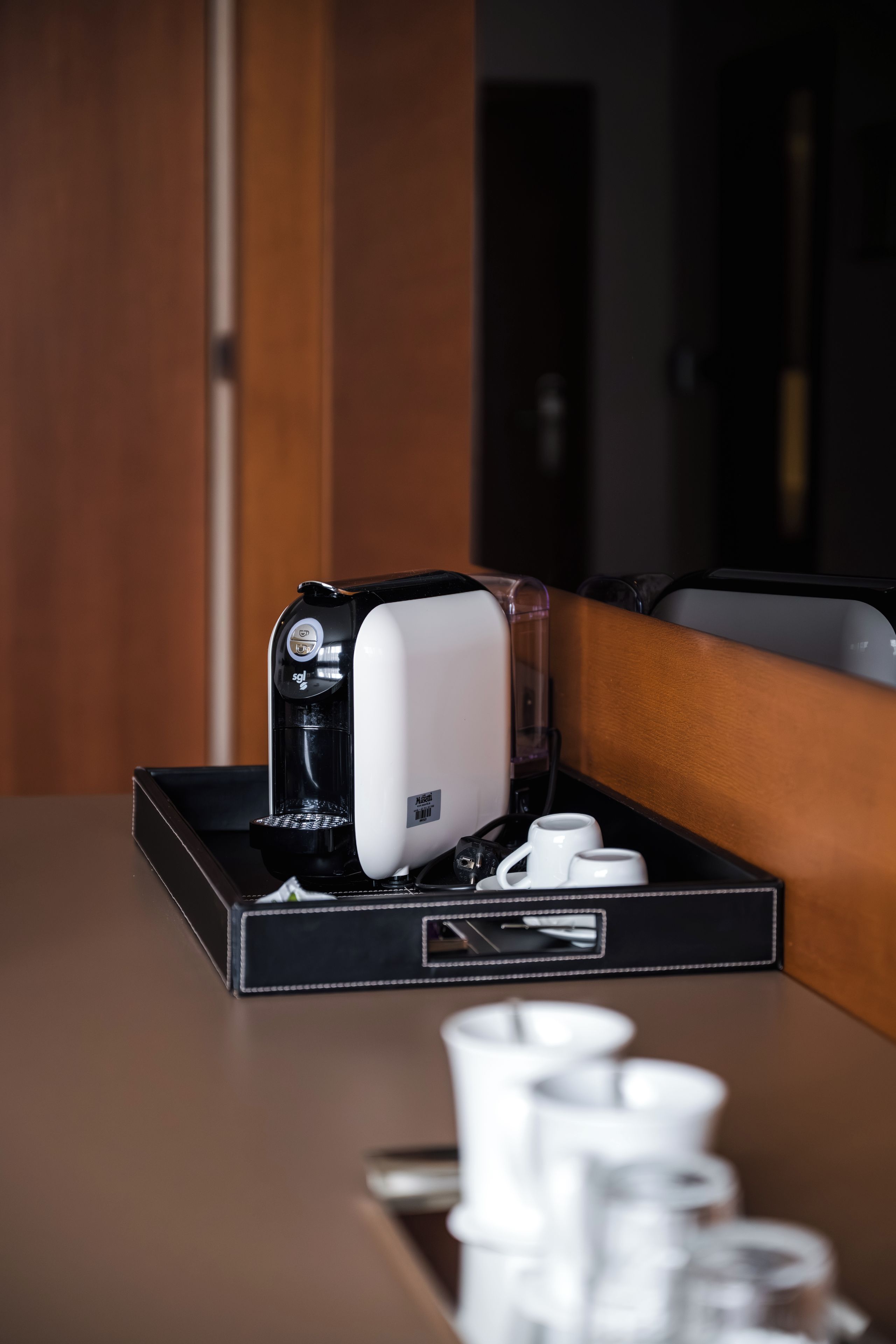 A coffee machine on a table with a tray, two white cups, and a smartphone.