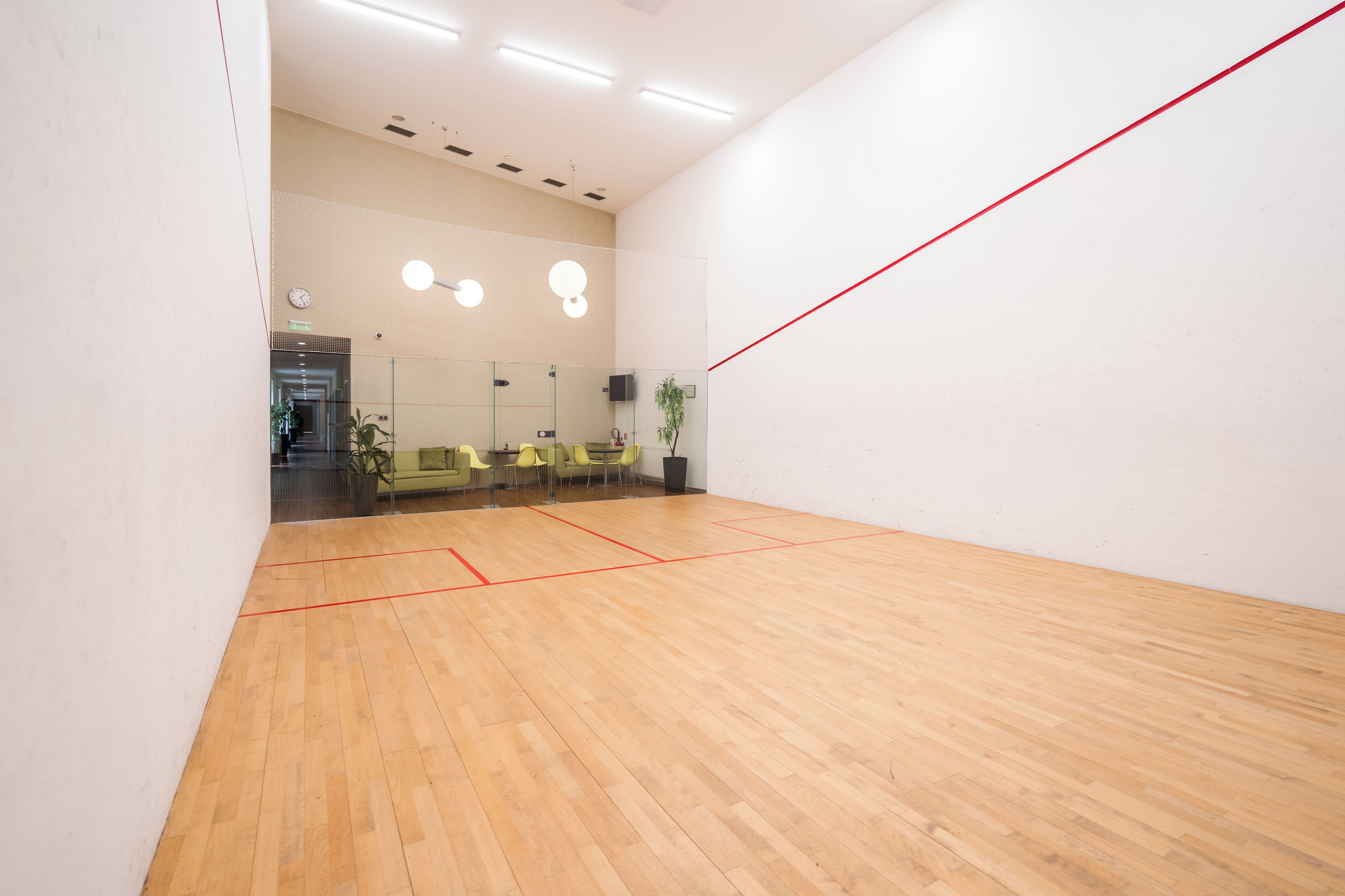 A squash court with wooden flooring and red boundary lines.