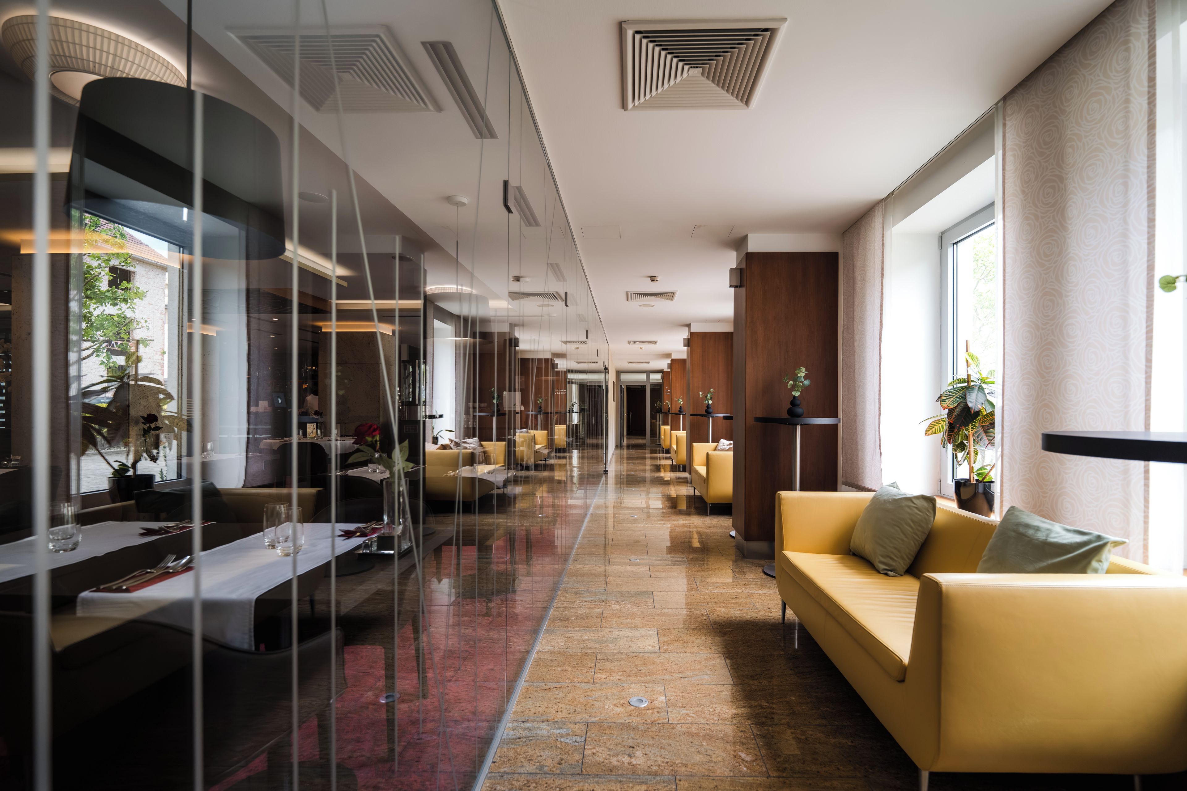 Un vestíbulo de hotel con un separador de vidrio, una recepción, un sofá y una planta.