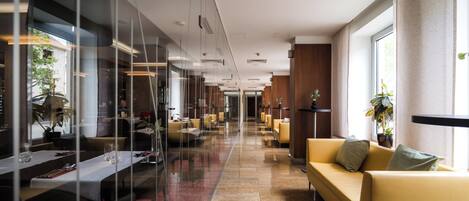 Un vestíbulo de hotel con un separador de vidrio, una recepción, un sofá y una planta.