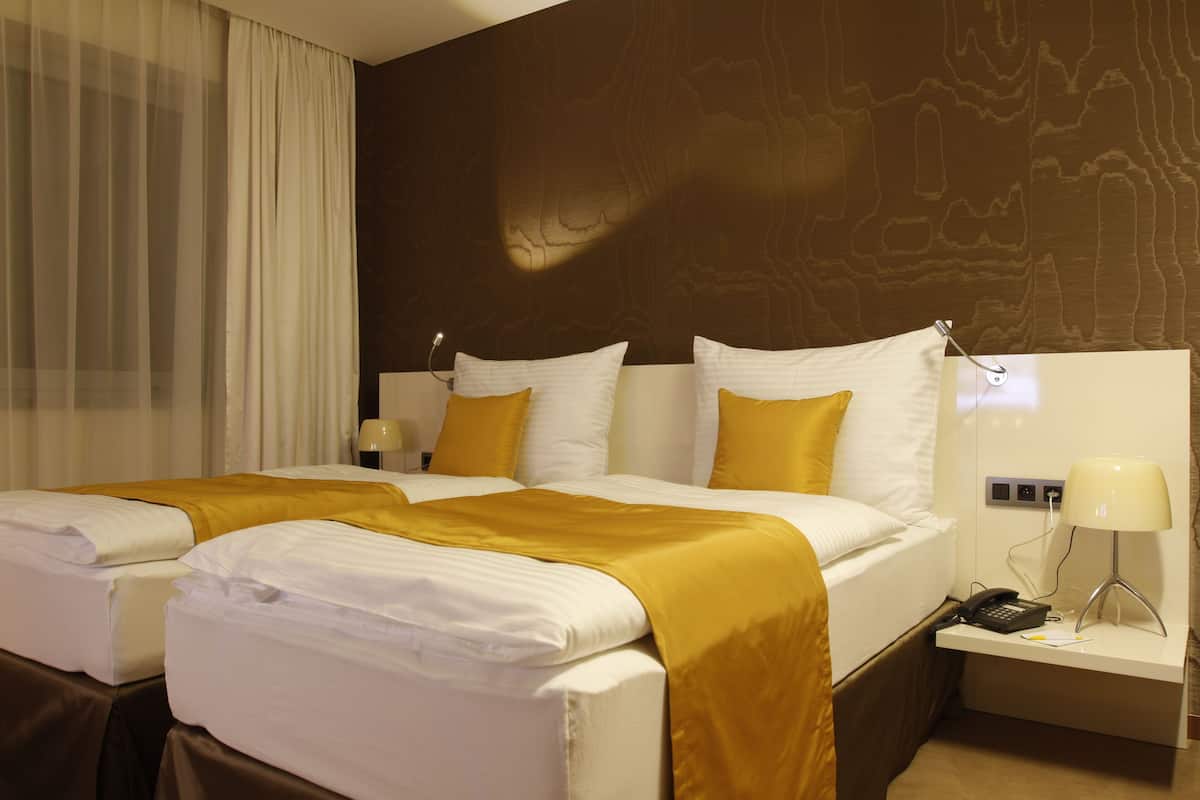 A hotel room with two beds, a nightstand with a lamp, and a wall with a wood-like pattern.