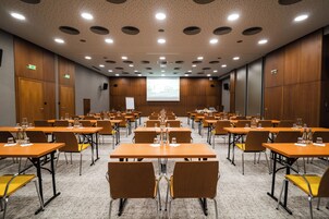 Un salón de conferencias con varias mesas, sillas y una pantalla grande.