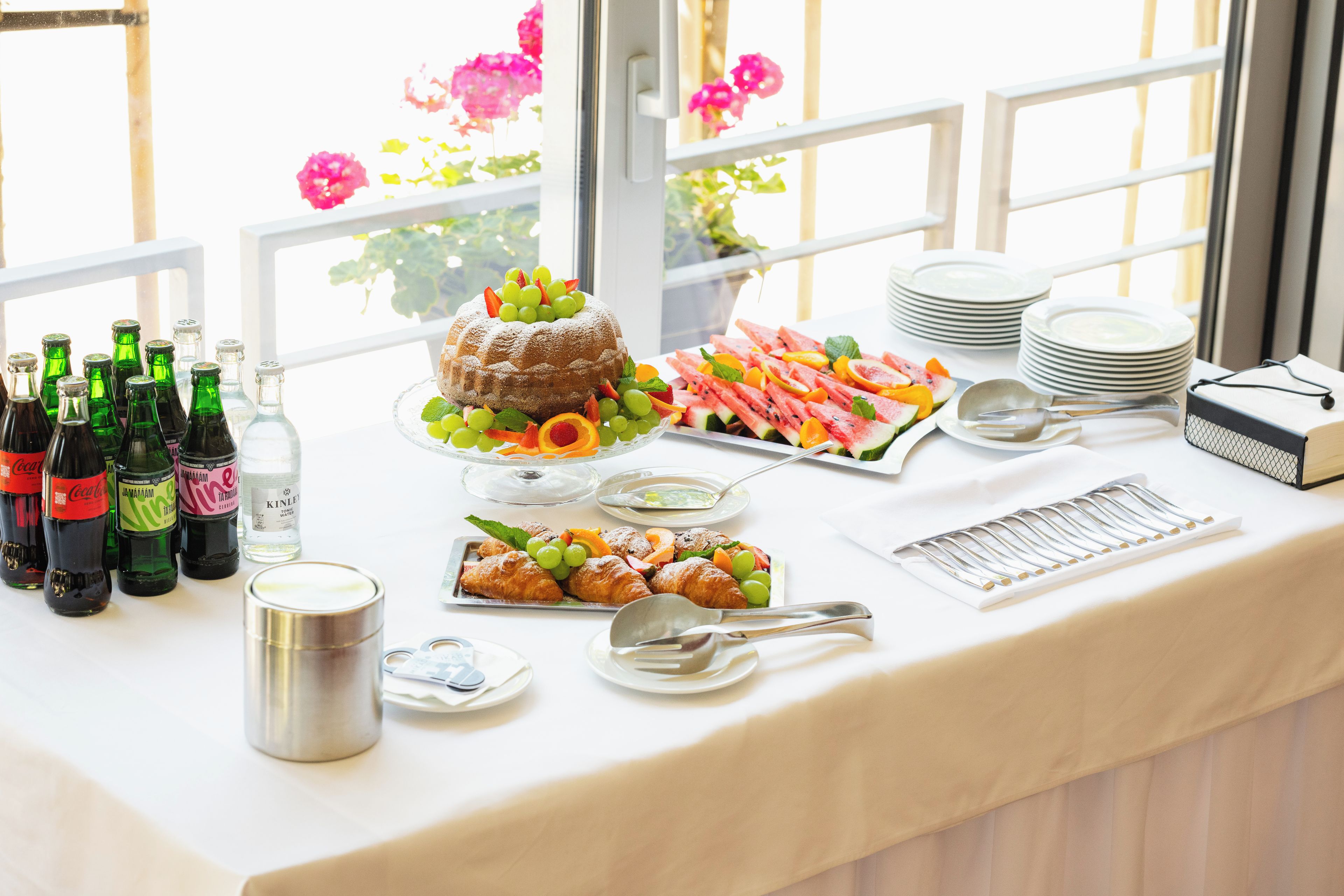 A buffet table with various food items, including a cake, fruits, and pastries, along with bottles of beverages.