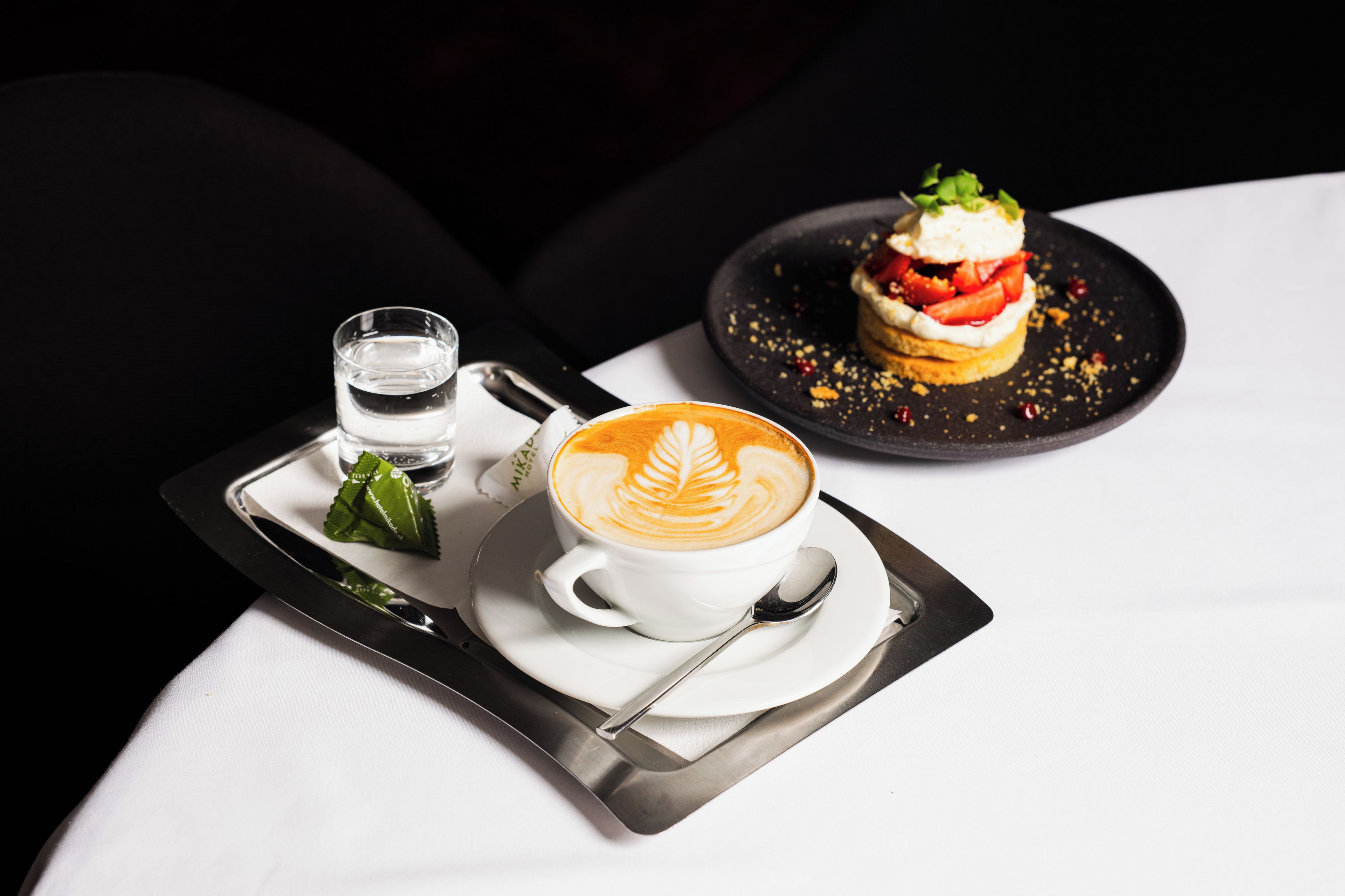 Un plateau avec une tasse de café, un verre d’eau et un dessert, posé sur une table.