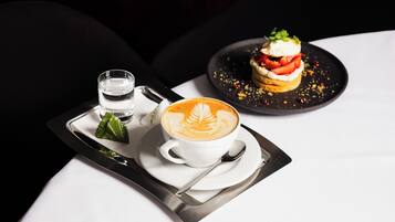 Un plateau avec une tasse de café, un verre d’eau et un dessert, posé sur une table.