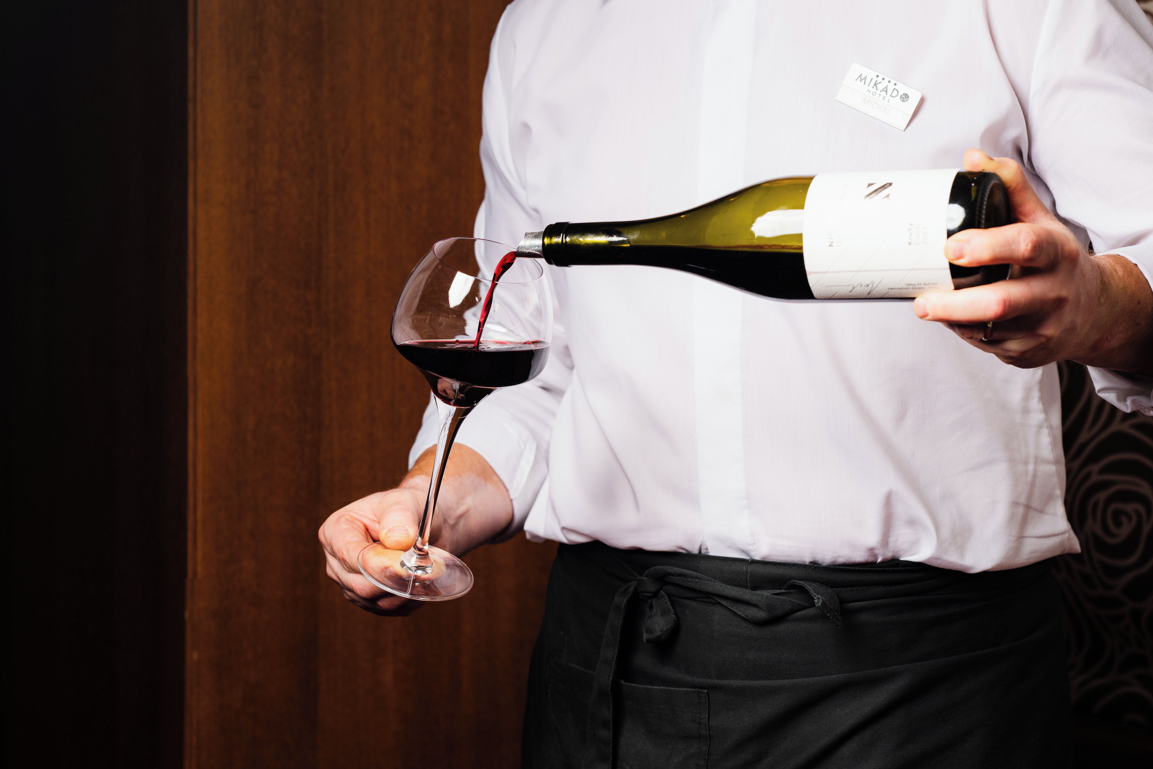 A person pouring red wine from a bottle into a glass.